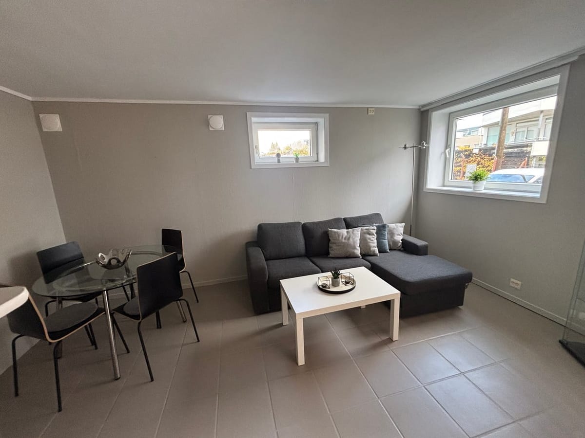 Stua med sofa, spisebord og to vinduer mot gaten